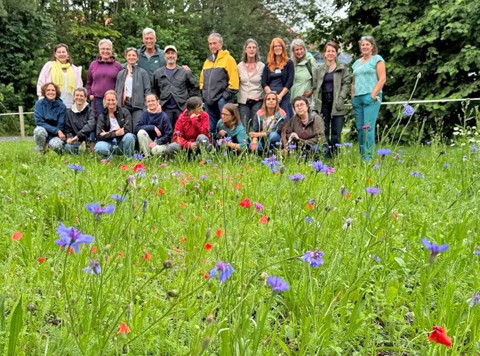 Gruppenfoto der Teilnehmenden des Blühbotschafter:innen-Lehrgangs 2024 auf ihrer selbst angelegten Blühfläche mit Kornblumen und Klatschmohn.