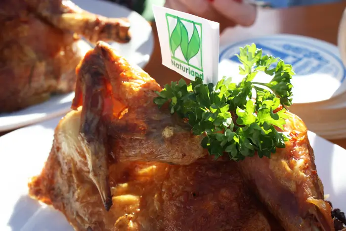 Auf einem halben gegrillten Wiesnhendl liegt Petersilie, daneben steckt eine kleine Naturland-Papierflagge.