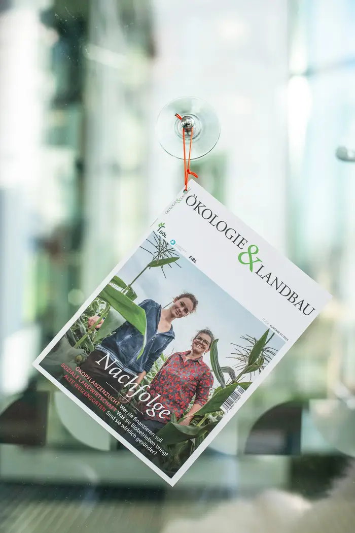 Die Zeitschrift Ökologie und Landbau mit dem Titelthema "Nachfolge" hängt mit einem roten Band an einem selbstklebenden Haken an einer Glaswand.