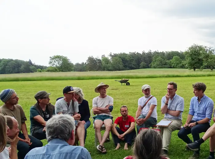 Menschen sitzen im Kreis auf Stühlen auf einer Wiese.